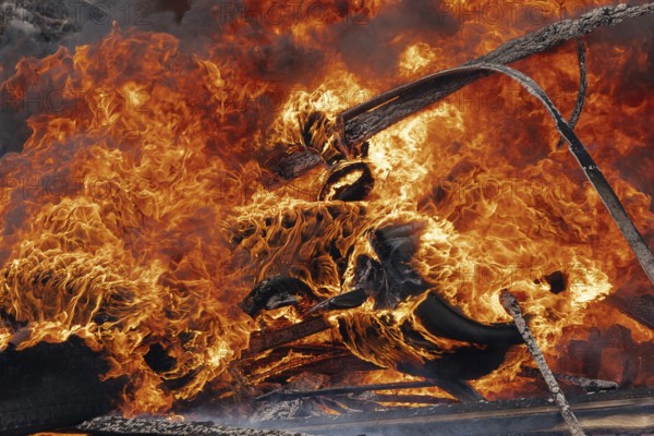 Burning cars wheels, strong flame of red-orange fire and clouds of black fumes. Selective focus, blur from strong fire