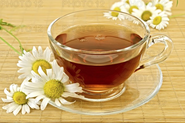 Herbal tea in a glass cup with saucer, camomile on a background of bamboo napkins