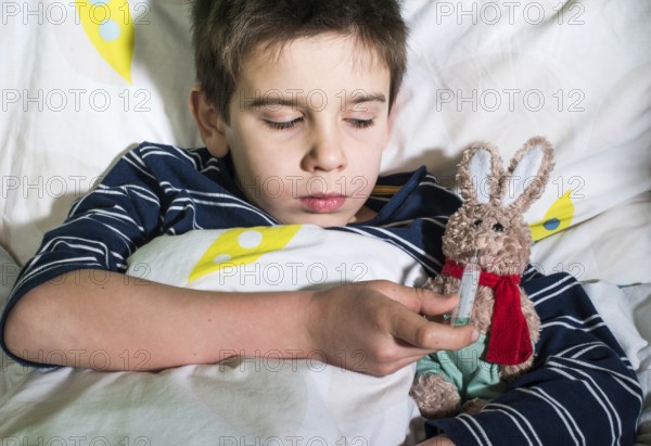 Sick child in bed with teddy bear. Measuring the temperature with a thermometer