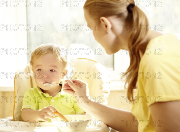 Young mother is feeding her two year old boy with porridge