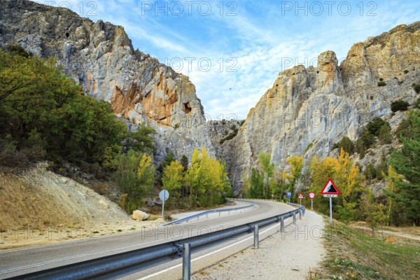The trip to Spain. Asphalt highway passes among steep cliffs. The sky is covered with light clouds. Huge gray rocks illuminated by sunset