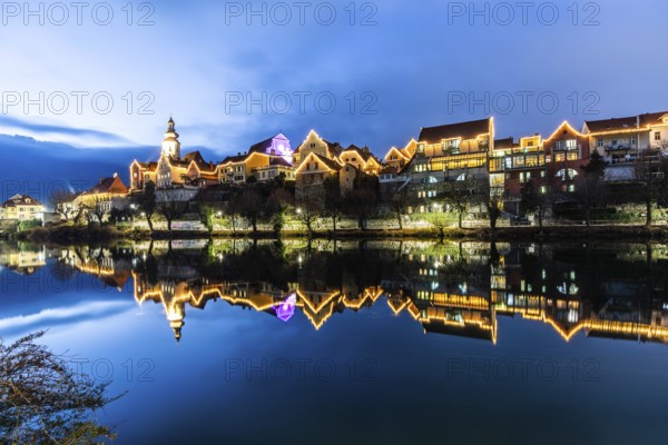 Christmas illuminated house facade of Frohnleiten reflected in the river Mur, blue hour, Frohnleiten, Styria, Austria