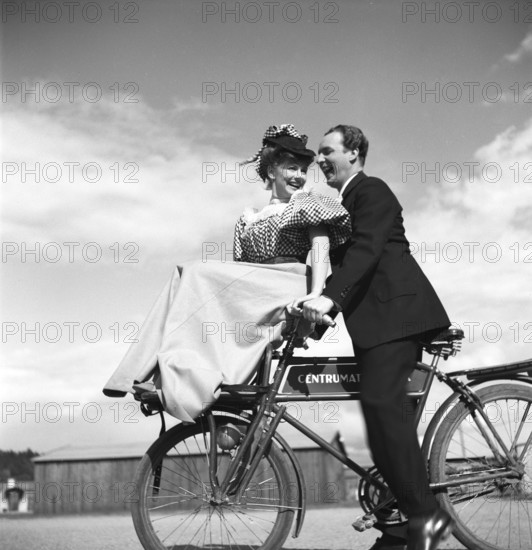 1940s couple on a bicycle. A young couple is riding their bicycles on a sunny day. They are both actors, Sonja Wigert and Arnold Sjöstrand and they have some fun while recording their new film. Sweden 1944. Photo Kristoffersson K23-6