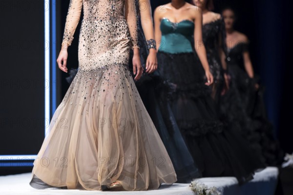 Female models walk the runway in beautiful designer dresses during a Fashion Show. Fashion catwalk event showing new collection of clothes. Unrecognizable people