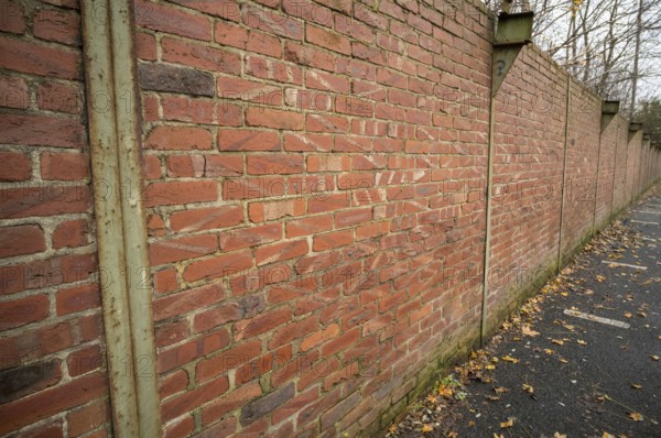 Red brick wall with metal supports and fallen autumn leaves on the ground beside a paved area