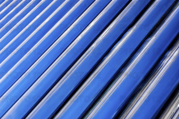 A diagonal and up close view of the convection tubes of a solar geyser as they fill the horizontal frame to create an abstract background image of blue and black diagonal lines