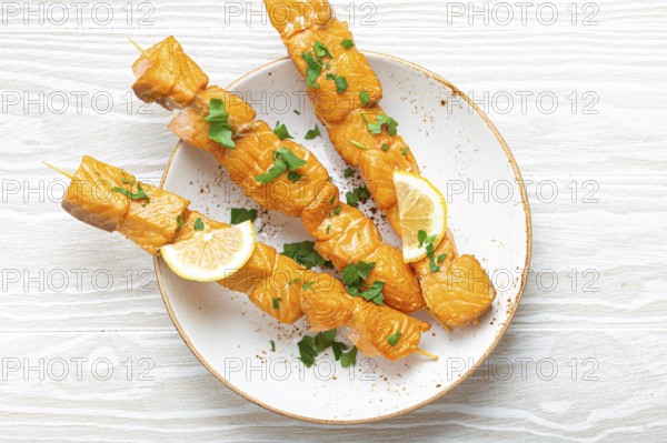 Grilled barbecue salmon skewers seasoned with green parsley and lemon on ceramic plate on white wooden rustic table background top view, healthy eating, food photography, food photography