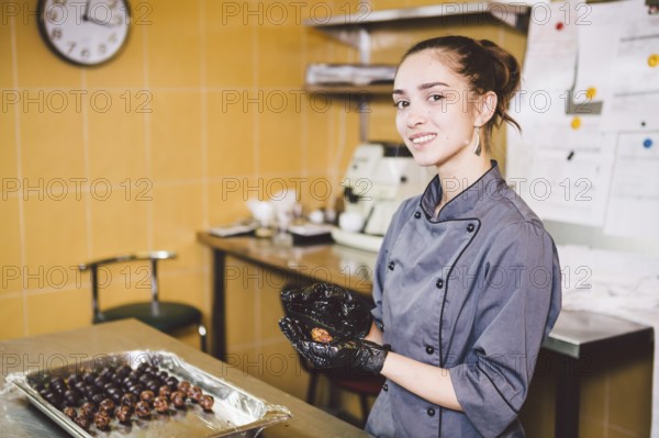 Subject profession and cooking pastry. young Caucasian woman with tattoo of pastry chef in kitchen of restaurant preparing round chocolate candies handmade truffle in black gloves and uniform