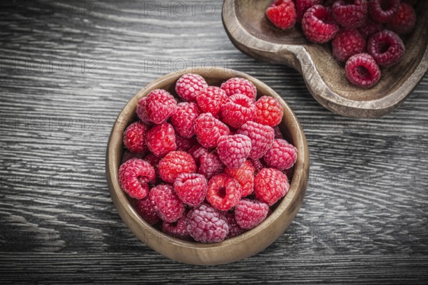 Round and heart-shaped bowls with ripe raspberries on wooden board