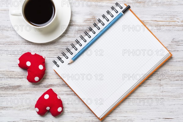 Coffee cup notepad pencil and two red hearts on wooden surface