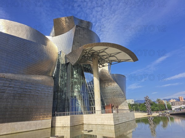 Futuristic building with curved metal shapes under a blue sky reflects innovative architecture, bilbao, spain