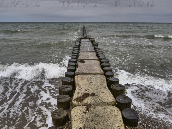A long jetty leads into the sea, surrounded by waves and a cloudy sky, ahrenshoop, zingst, Baltic Sea, Germany