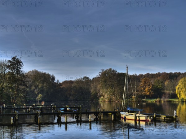 Several boats on a calm autumn lake, framed by trees and jetties, under a blue sky, Borken, münsterland, germany