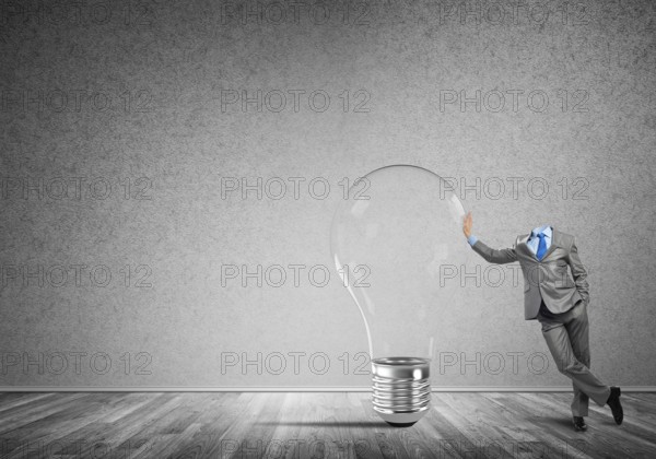 Headless businessman in empty room leaning on glass light bulb