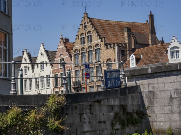 Historic brick buildings along a canal with a railing in the foreground and blue sky, Bruges, Flanders, Belgium