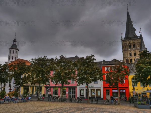 Colourful houses on the market square with a church and church towers in the background under a gloomy sky, Xanten, North Rhine-Westphalia, Germany