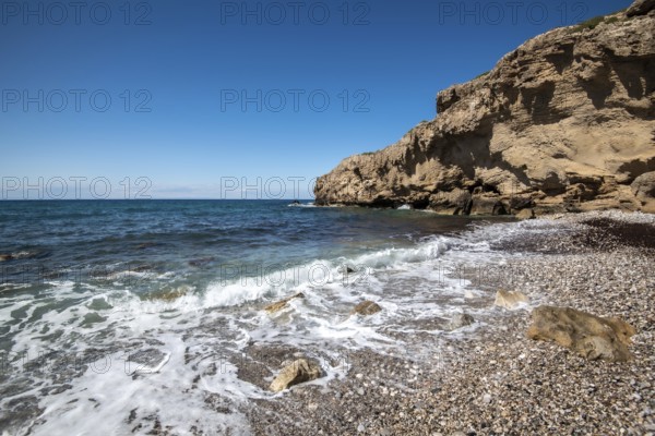 Empty pebble tropical beach under white cliffs against blue sky. Copy space