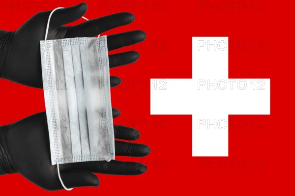 Doctor holds face mask in hands in black medical gloves on background colors flag of Switzerland. Concept coronavirus quarantine, pandemic outbreak, grippe, airborne diseases. Human respiratory mask