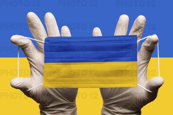 Doctor holding in white gloves protection medical face mask with National flag of Ukraine superimposed on mask. Concept coronavirus disease SARS-CoV-2 pandemic on background of National Ukrainian flag