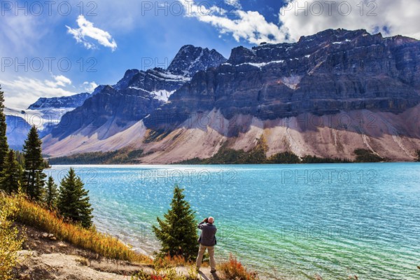 The Majestic Rockies of Canada. A gray-haired tourist photographs a grandiose landscape. Lake Bow is surrounded by cliffs and glaciers. The concept of active, environmental and photo tourism