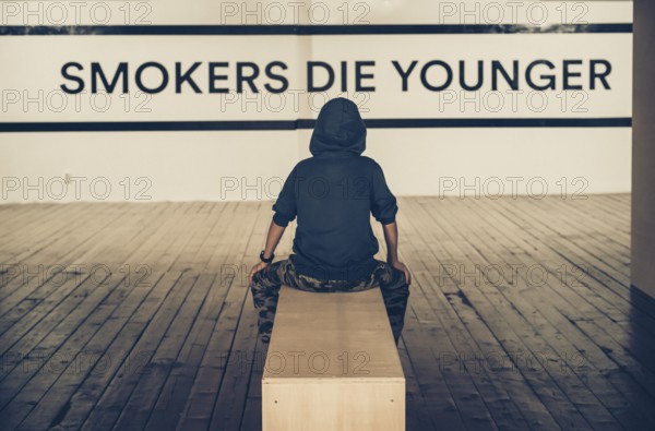 Teenager smoking and message on wall - Smokers die younger. No smoking concept with child. Casual clothes