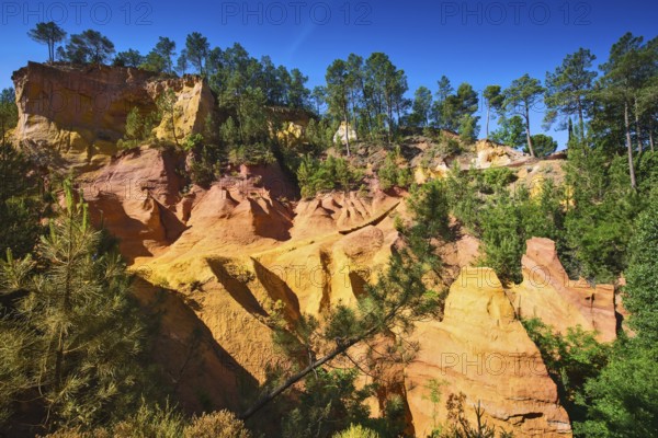 Unique red and orange hills in the province of Languedoc - Roussillon, France. Green trees create a beautiful contrast with the bright ocher