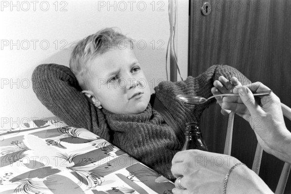 A boy is sick and won't take his medicine. His mother holds out a spoon and waits for him to gape and take it, but he keeps his mouth shut. An everyday life event that today would look the same, the medicine sometimes does not taste so good. Sweden 1956. Conard ref 3157