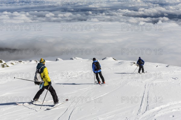 Three free riders are prepairing for skiing down a snowy rocky mountain top
