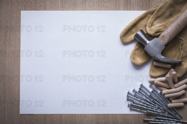Clean sheet of paper steel nails claw hammer wooden dowel pins and leather safety gloves on wood board copyspace construction concept