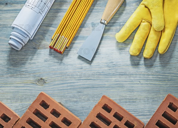 Assortment of red bricks safety gloves palette knife blueprints wooden meter building concept