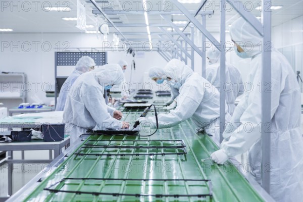 Factory workers in white lab suits and face masks, producing tv sets on a green assembly line with some modern equipment