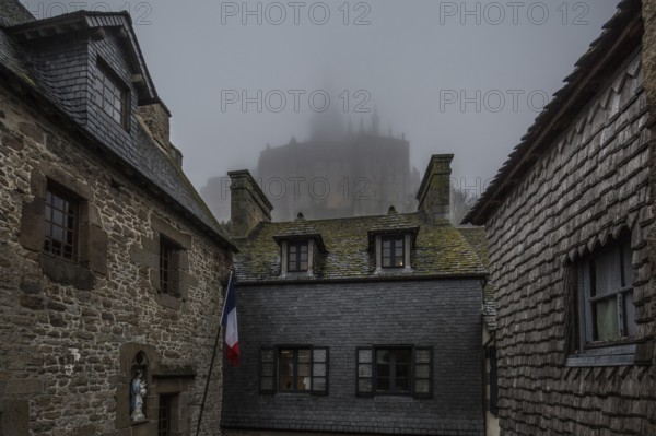 Mont-Saint-Michel, monastery hill, houses at the lower end of the Grande Rue above the abbey in the fog