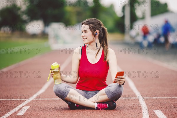 Beautiful fitneß girl uses smartphone at stadium after workout. Sports and healthy. Sport woman use of cellphone inside sport complex. Sport and technology. resting after workout, run at red track