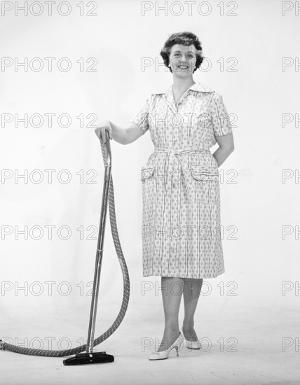 Cleaning day in the 1960s. A woman is standing holding a vacuum cleaner, looking happy. Sweden 1960s Kristoffersson ref CN109-10