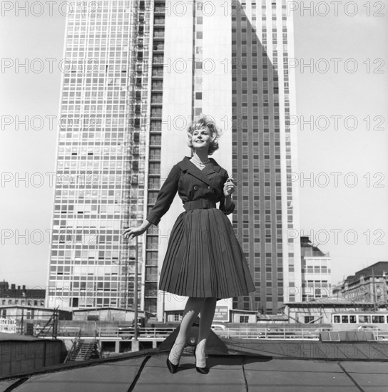 In the 1950s. A woman modelling a 1950s outfit with a jacket and skirt in matching dark. In the background the newly finished skyscraper housing the swedish tax offices. Sweden 1959 Kristoffersson ref CH21