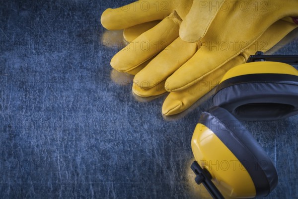 Noise reduction yellow headphones and leather protective gloves on scratched metallic background construction concept
