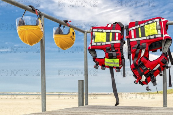 Safety helmets and life jackets hanging on railing near beach at coast