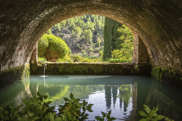 Tranquil, arched tunnel with views of water and trees in the background, Jardines de Alfabia gardens, Bunyola, Majorca, Spain