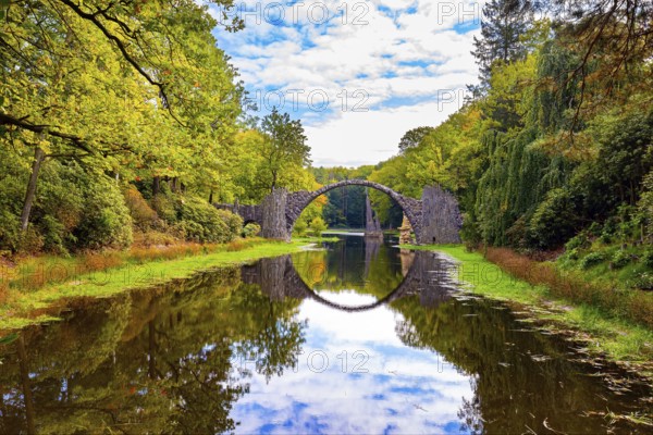 The Devil's Bridge on the Rakots River. Park Kromlau, Germany. The basalt columns of the bridge form a perfect circle with their reflection in the water. Picturesque narrow bridge in the park
