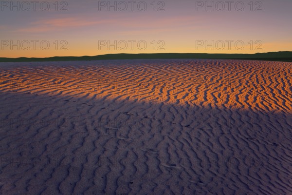 Orange sunset in the desert. Mesquite Flat Sand Dunes, California. The gentle slopes of the sand dunes are rippled by the wind. Concept of active, ecological and photo tourism