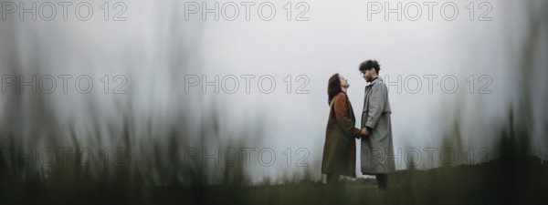 A couple standing apart in a field on an overcast day, holding hands, conveying a sense of connection
