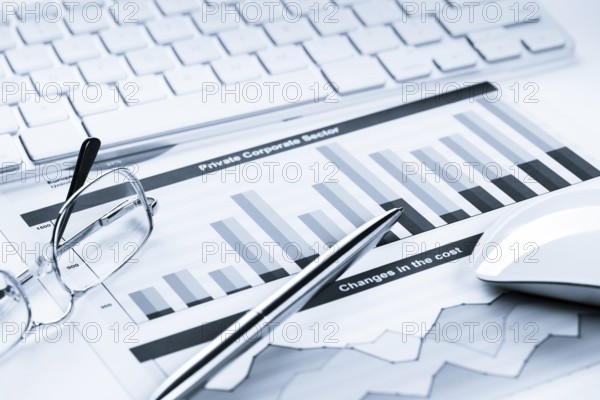Business workplace with keyboard glasses and financial documents on table