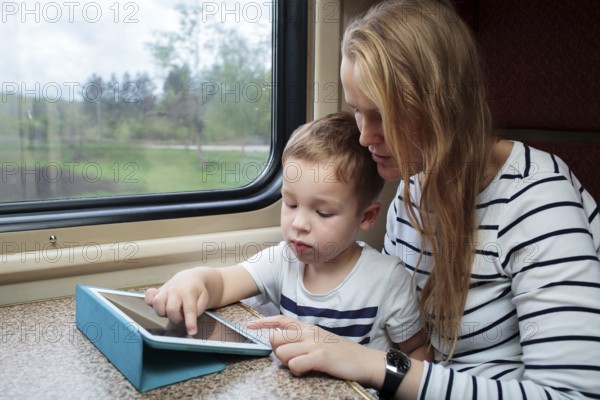 Mother and her little son using touchpad sitting by the window in the train