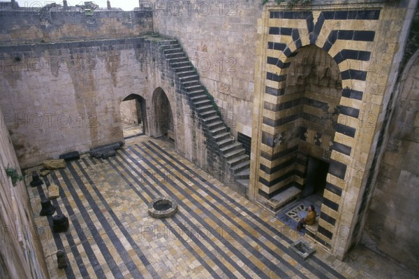 The Citadel of Aleppo is a large medieval fortified palace in the centre of the old city of Aleppo, northern Syria. It is considered to be one of the oldest and largest castles in the world. Usage of the Citadel hill dates back at least to the middle of the 3rd millennium BCE. Subsequently occupied by many civilizations including the Greeks, Byzantines, Ayyubids and Mamelukes, the majority of the construction as it stands today is thought to originate from the Ayyubid period.<br/><br/> Aleppo, the second city of Syria and quite possibly the longest continually inhabited settlement in the world, is of venerable age. So old, indeed, that its Arabic name, Halab, is first mentioned in Semitic texts of the third millennium BCE. Situated in the north-west of the country, just a few kilometres from the Turkish frontier, Aleppo is located at the confluence of several great trade routes and, as a city of commerce, has always been rich