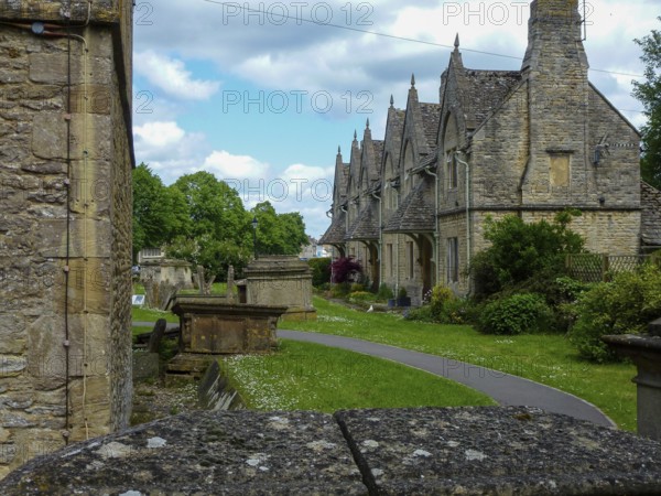 Charming cotswold stone houses stand alongside a serene cemetery, showcasing the timeless beauty of traditional english architecture