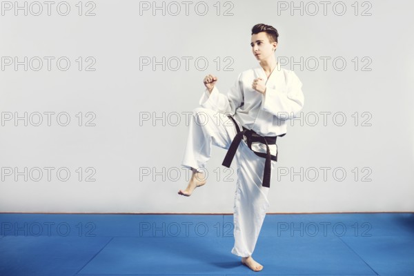 Girl in karate suit kimono in studio at grey background. Female child shows judo or karate stans in white uniform with black belt. Individual martial art sport . Full body portrait