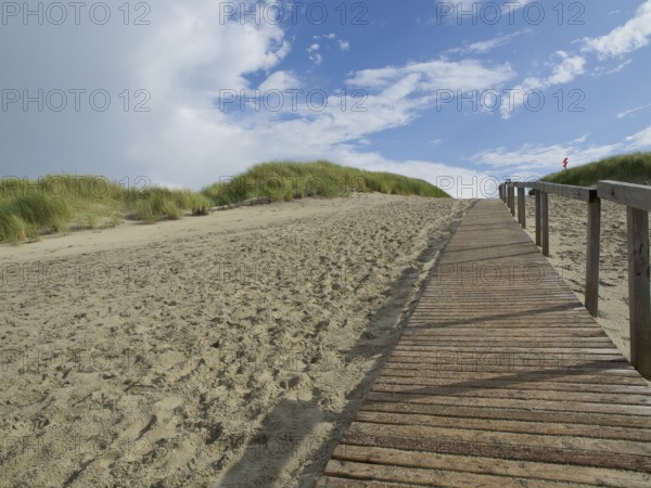 A long wooden walkway leads up sandy dunes, with a sky of clouds and blue, Juist, East Frisia, Germany