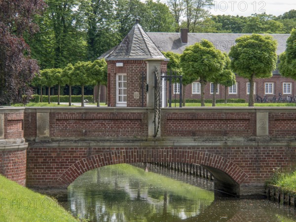 A brick bridge over a body of water, surrounded by manicured hedges and a castle complex, nordkirchen, münsterland, germany