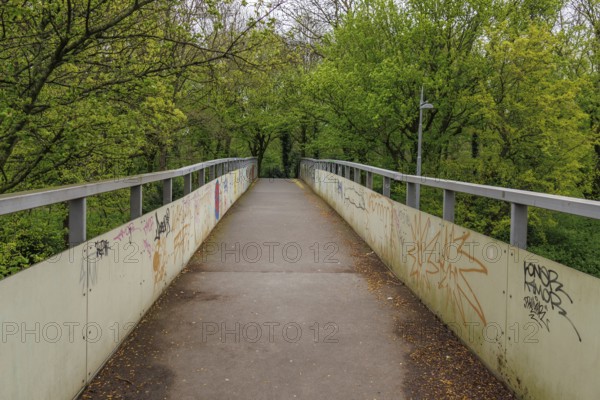 Pedestrian bridge with graffiti on the sides, surrounded by green trees, Rotterdam, Netherlands
