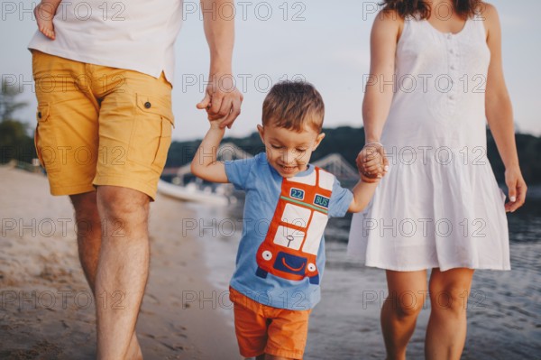 Family holiday in summer. Young Caucasian family foot walking barefoot sandy beach, shore river water. Dad mom holding hands two children, brothers. Big friendly family with two children near lake
